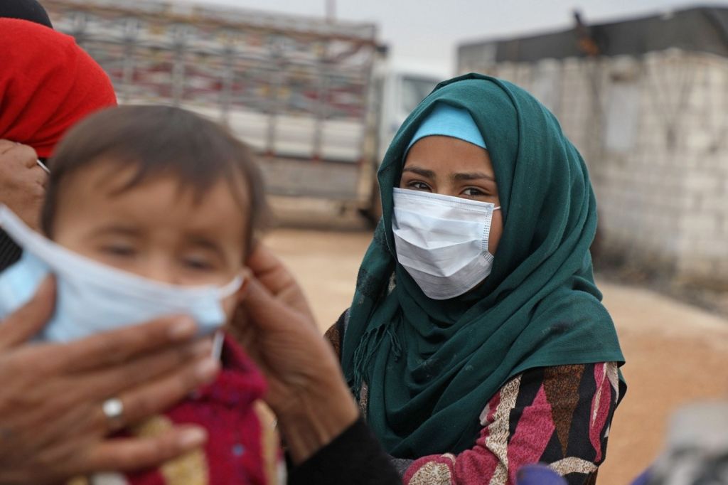 マスクを着けている黒人女性と、周りの人にマスクを着けられている小さな子供