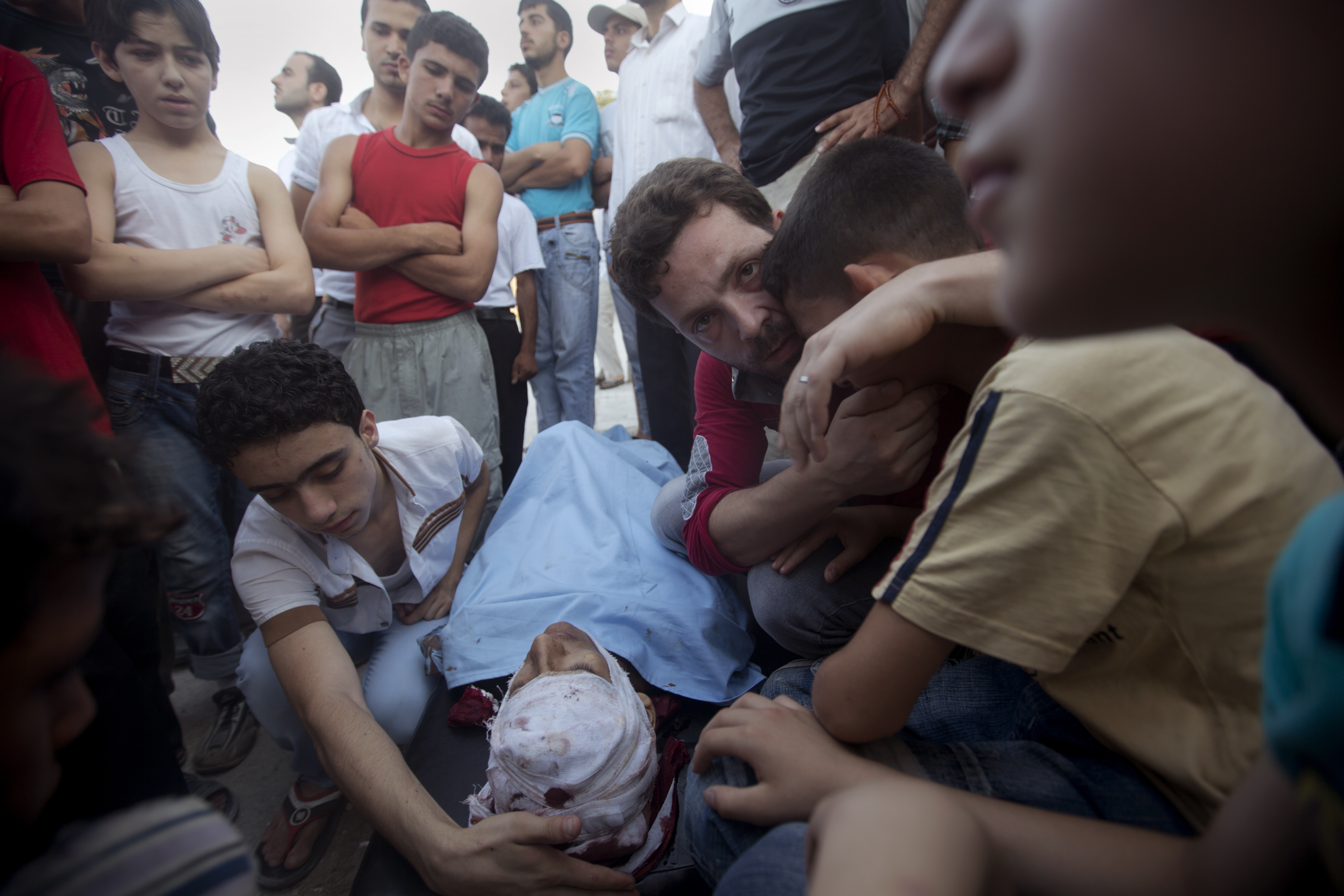 亡くなった息子を前に嘆き悲しむもう一人の息子を抱きしめ、こちらを見つめる父親